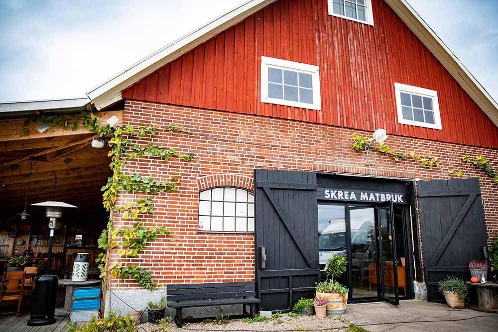 Fasaden och entrén till Skrea Matbruk, tegelbyggnad med rött trä och svarta portar.