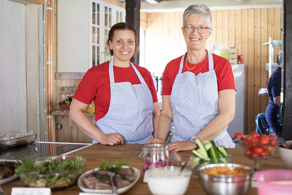 Två kvinnor med förkläden står framför serveringsfat.