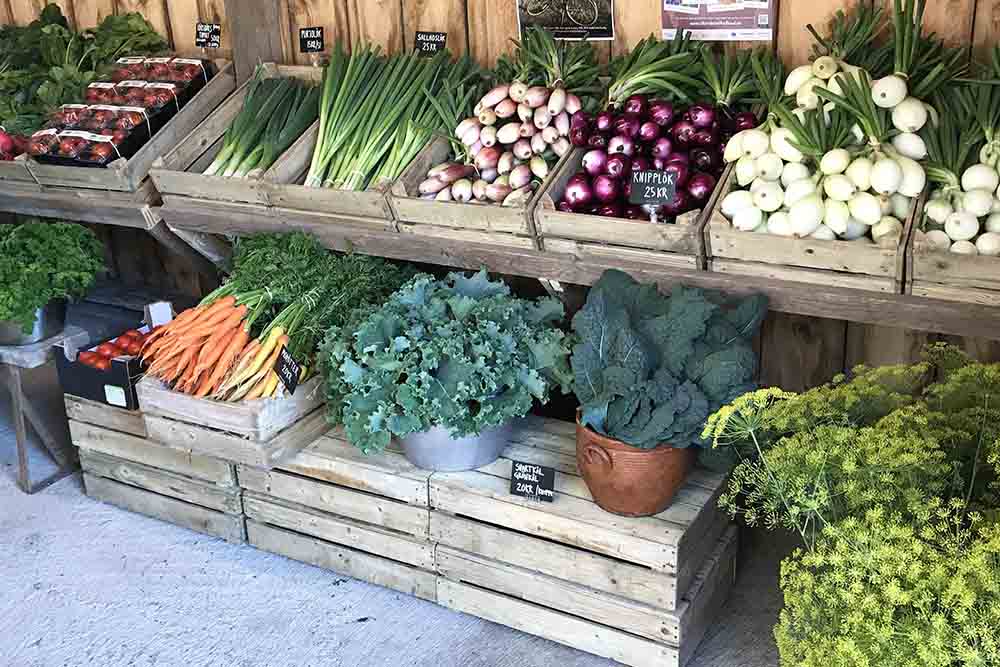 Gårdsbutik med grönsaker i trälådor.